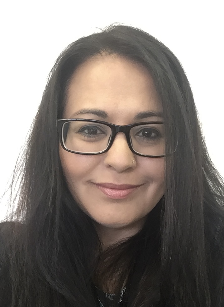 Head shot of Roopa Master-Coles looking directly at you. Her long, black hair is straight, and she wears black rimmed glasses.